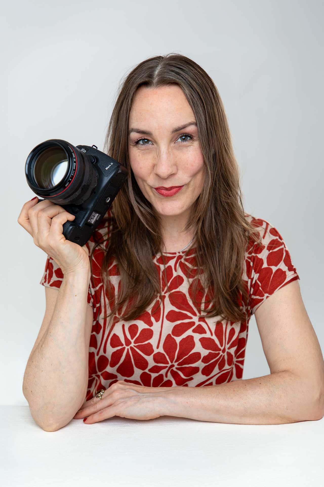 Frauen-Empowerment-Fotoshooting-Hamburg-Dagmar-Tanamal Frau die verschmitzt guckt, eine Kamera in der Hand hat und am Tisch sitzt